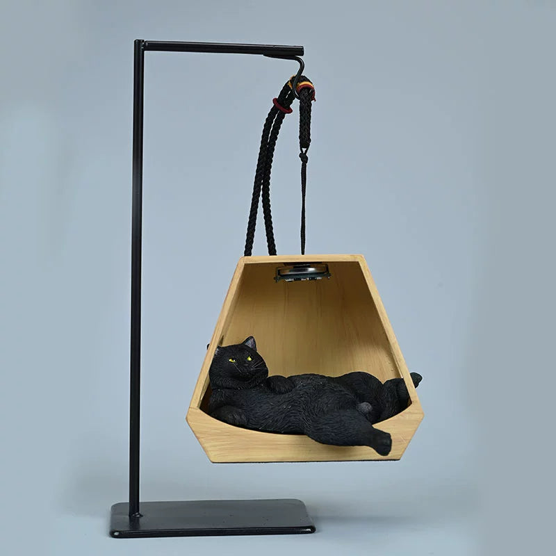 A whimsical decorative piece featuring a cat model lounging comfortably in a hanging basket shaped like a wooden hexagon. The basket is suspended from a metal frame with ropes, illuminated by a small overhead light, enhancing the cozy and serene appearance of the cat. This charming figurine adds a playful touch to any space.
