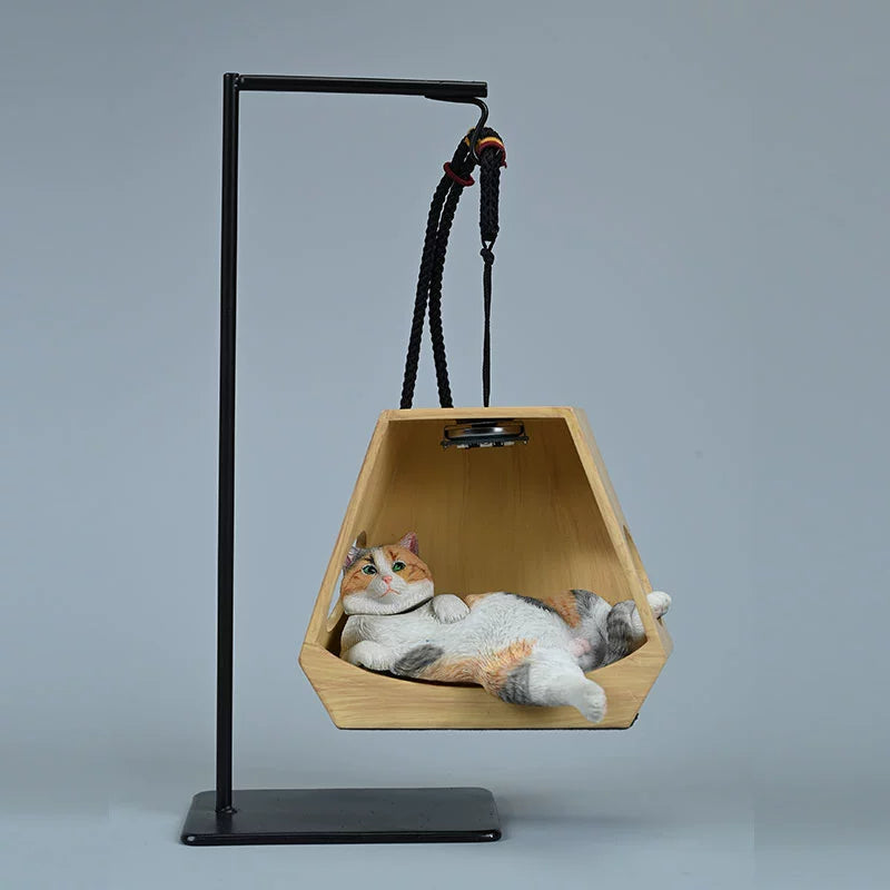 A whimsical decorative piece featuring a cat model lounging comfortably in a hanging basket shaped like a wooden hexagon. The basket is suspended from a metal frame with ropes, illuminated by a small overhead light, enhancing the cozy and serene appearance of the cat. This charming figurine adds a playful touch to any space.