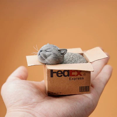 A pair of adorable cat figurines comfortably nestled inside small FedEx delivery boxes. Each cat, with eyes closed and a serene expression, appears to be sleeping soundly. These lifelike models are a delightful representation of contentment and cuteness, perfect for any cat lover's collection.