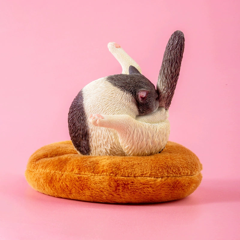 "A set of five 1/6 scale cat models humorously designed to resemble chicken legs. Each cat is curled up in a round, resting position on a plush, brown cushion, showcasing different fur colors and patterns, including grey, black and white, orange, and cream."