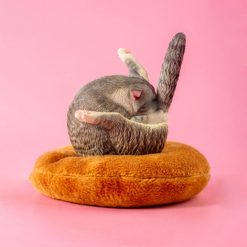 "A set of five 1/6 scale cat models humorously designed to resemble chicken legs. Each cat is curled up in a round, resting position on a plush, brown cushion, showcasing different fur colors and patterns, including grey, black and white, orange, and cream."
