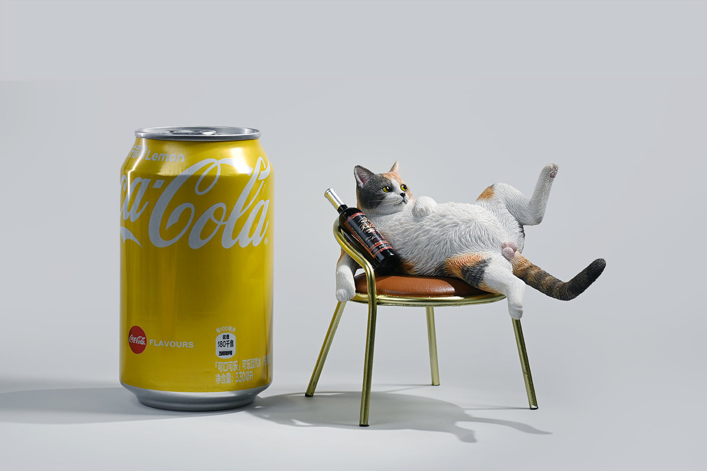 A 1/6 scale figurine of an orange tabby cat lounging on a chair with a bottle, portraying a humorous 'drunk' pose.