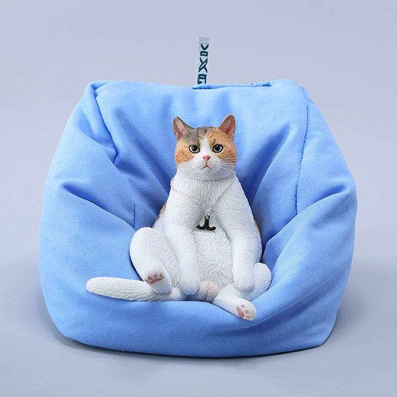 A set of four realistic 1/6 scale lazy cat figurines in different colors, each sitting comfortably with a lifelike expression. The cats are depicted in various coats: calico, grey tabby, orange tabby, and black. One figurine is shown lounging on a blue beanbag, adding to the whimsical charm of the collection.