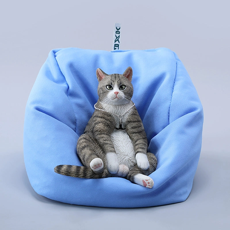 A set of four realistic 1/6 scale lazy cat figurines in different colors, each sitting comfortably with a lifelike expression. The cats are depicted in various coats: calico, grey tabby, orange tabby, and black. One figurine is shown lounging on a blue beanbag, adding to the whimsical charm of the collection.