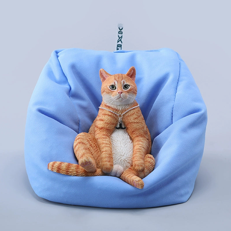 A set of four realistic 1/6 scale lazy cat figurines in different colors, each sitting comfortably with a lifelike expression. The cats are depicted in various coats: calico, grey tabby, orange tabby, and black. One figurine is shown lounging on a blue beanbag, adding to the whimsical charm of the collection.