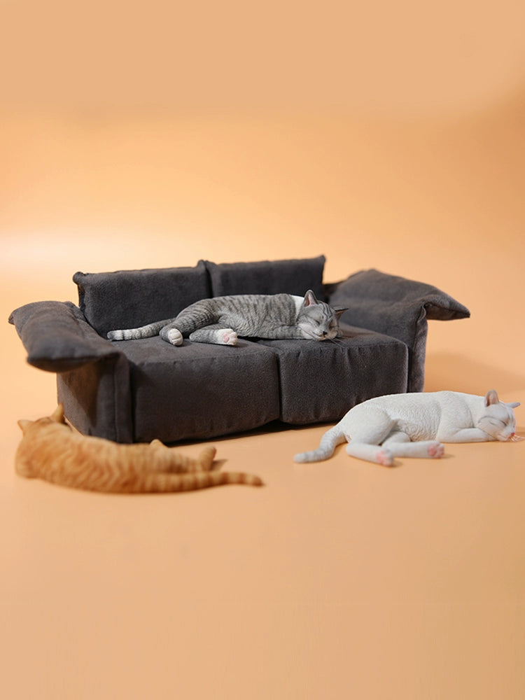 A realistic 1/6 scale model of a relaxed gray cat sleeping on a soft, gray couch, accompanied by two other cat figures lying nearby. The cat figures are detailed with life-like features, capturing their lazy and content postures, perfect for collectors and cat enthusiasts.