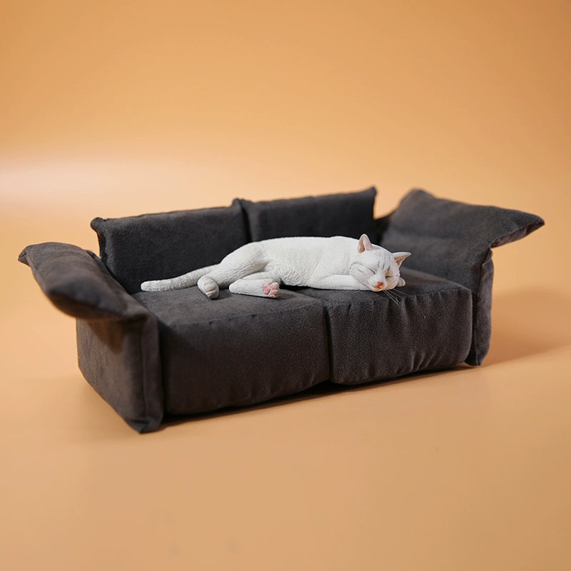 A realistic 1/6 scale model of a relaxed gray cat sleeping on a soft, gray couch, accompanied by two other cat figures lying nearby. The cat figures are detailed with life-like features, capturing their lazy and content postures, perfect for collectors and cat enthusiasts.