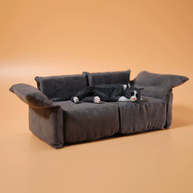 A realistic 1/6 scale model of a relaxed gray cat sleeping on a soft, gray couch, accompanied by two other cat figures lying nearby. The cat figures are detailed with life-like features, capturing their lazy and content postures, perfect for collectors and cat enthusiasts.