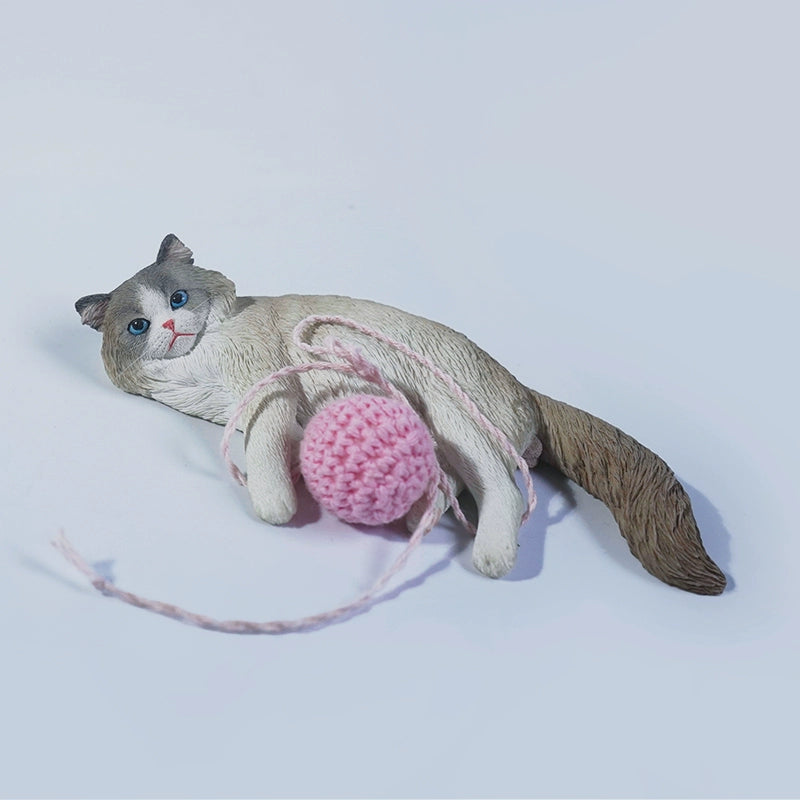 A lifelike 1/6 scale model of a Muppet Cat 3.0, featuring a cat laying on its side with a pink yarn ball. The model showcases detailed fur textures and bright blue eyes, capturing the playful and relaxed demeanor of the cat. Perfect for collectors and cat enthusiasts.