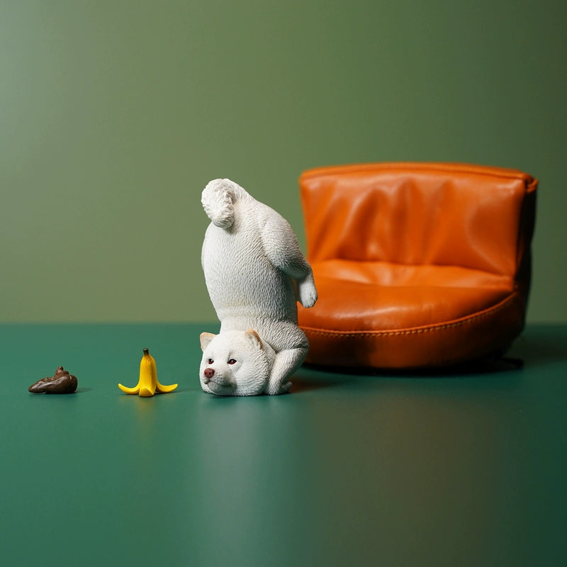 A charming 1/6 scale model of three Shiba Inu dogs, captured in a planking position. Each dog is distinctively colored - black, brown, and white, showcasing intricate detailing from their fur textures to their playful expressions, set against a green background.