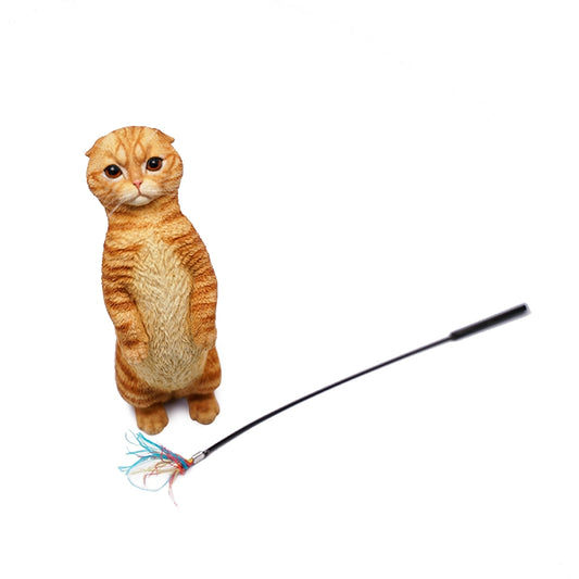 A 1/6 scale model of a Scottish Fold cat standing on its hind legs, with a toy wand featuring colorful feathers. The cat has an orange tabby coat and a curious expression.