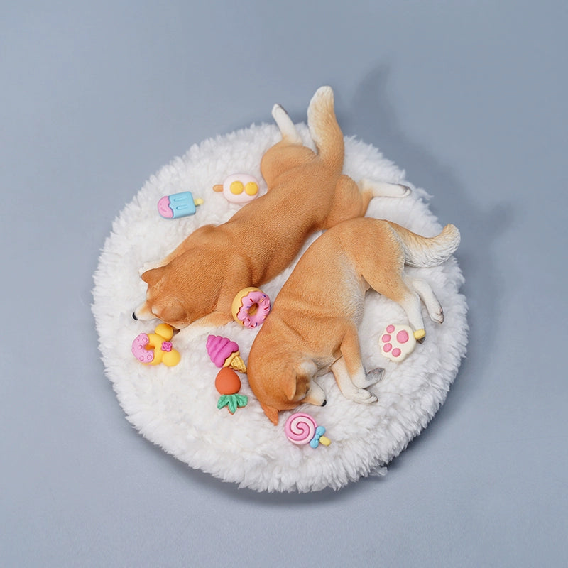 A detailed resin model of a sleeping Shiba Inu dog on a fluffy white bed, surrounded by colorful toy replicas like a carrot, ice cream cone, donut, and paw print. The model captures the serene essence of a Shiba Inu with its realistic fur texture and lifelike posture, ideal for collectors and dog enthusiasts.