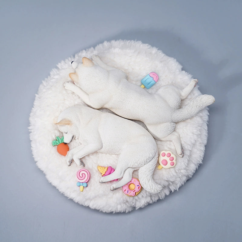 A detailed resin model of a sleeping Shiba Inu dog on a fluffy white bed, surrounded by colorful toy replicas like a carrot, ice cream cone, donut, and paw print. The model captures the serene essence of a Shiba Inu with its realistic fur texture and lifelike posture, ideal for collectors and dog enthusiasts.