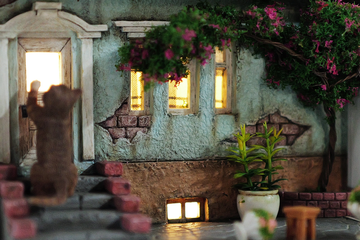 A detailed and charming art relief picture frame model featuring a white cat reaching up towards a window, surrounded by a beautifully crafted miniature garden with flowers, plants, and a rustic table with chairs. Perfect for adding a touch of whimsy and artistic flair to any room.