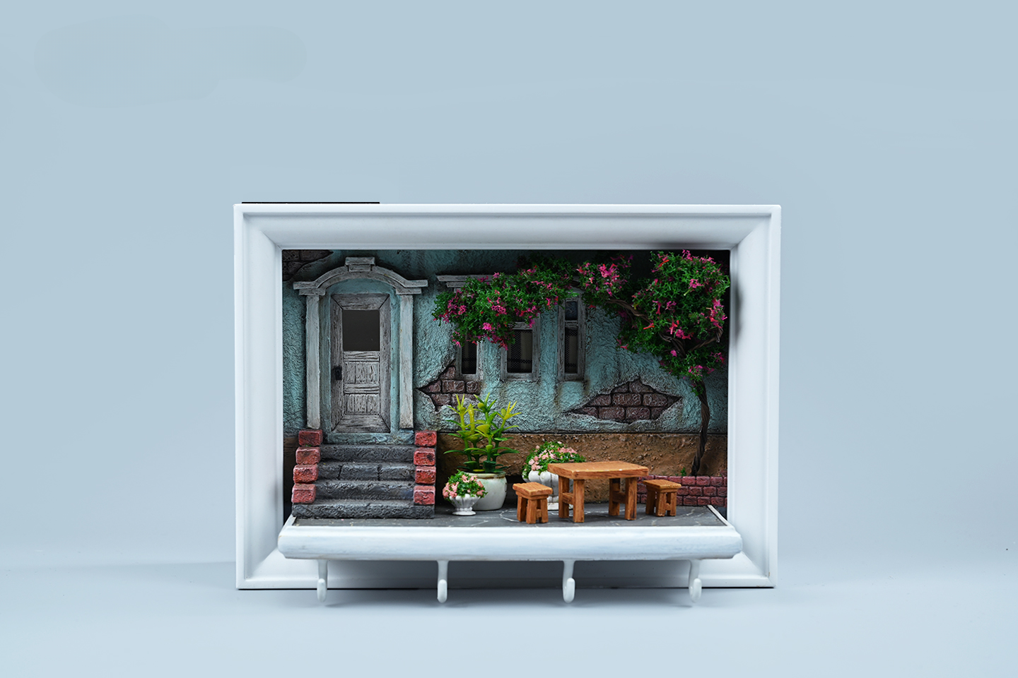 A detailed and charming art relief picture frame model featuring a white cat reaching up towards a window, surrounded by a beautifully crafted miniature garden with flowers, plants, and a rustic table with chairs. Perfect for adding a touch of whimsy and artistic flair to any room.