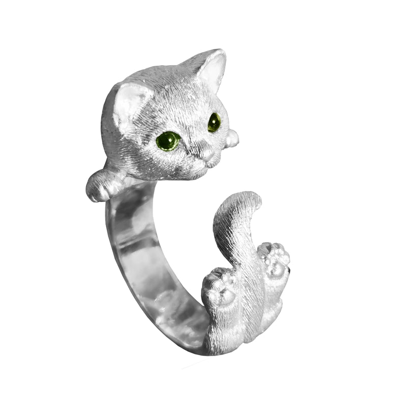 Close-up image of a handmade 925 sterling silver cat ring with blue gemstone eyes, highlighting the intricate details of the cat's face and the adorable tail wrapping around the finger. Matching earrings with similar detailing are also shown.