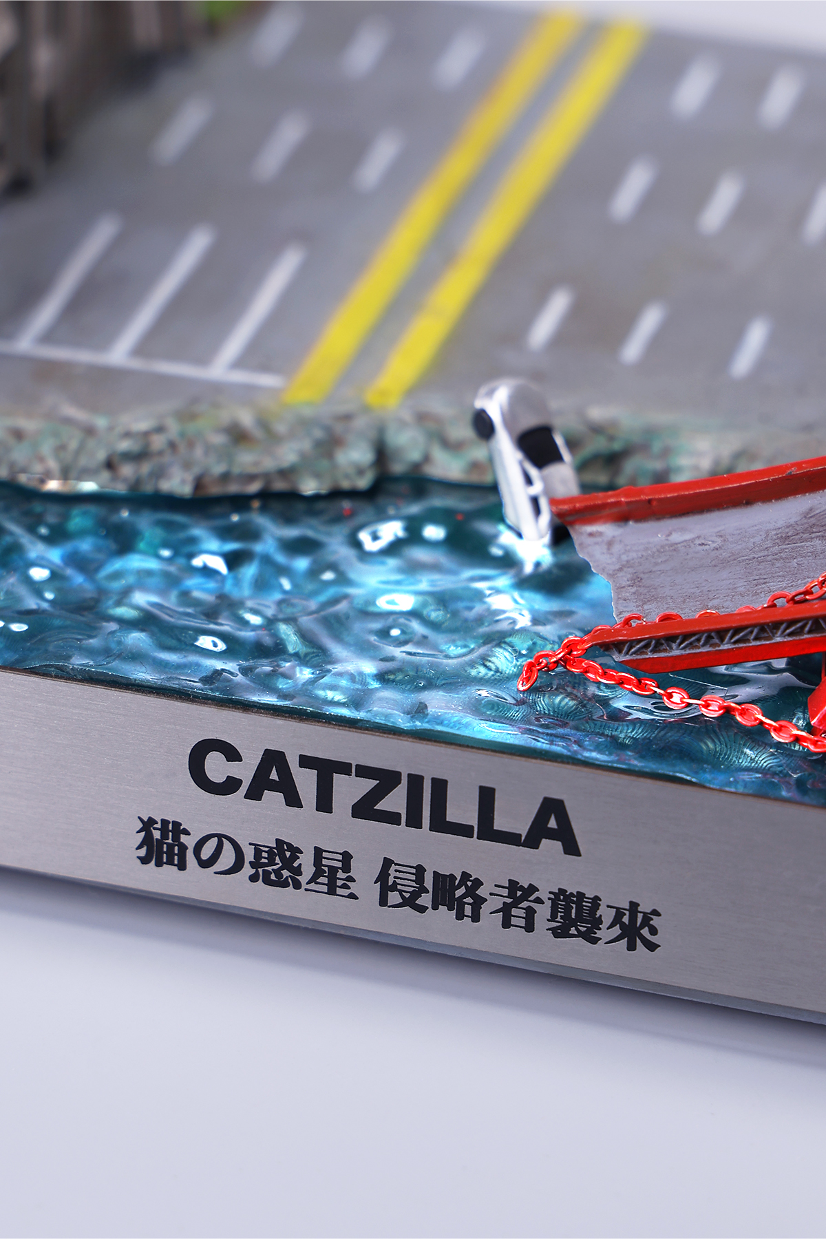 A striking model of Catzilla 2.0, showcasing a large, formidable cat figure breathing blue flames. The cat stands amid a miniature cityscape, featuring detailed buildings and structures, with another image displaying both the orange and black versions of the Catzilla model.