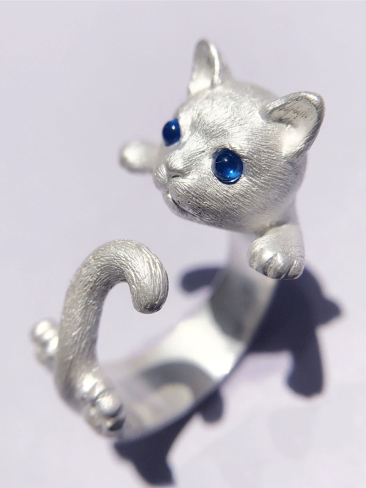 A handcrafted cat ring made of 925 sterling silver, featuring detailed fur textures and vibrant gemstone eyes, showcasing the playful pose of a kitten with its tail wrapped around the finger. Available in both silver and antique black finishes.