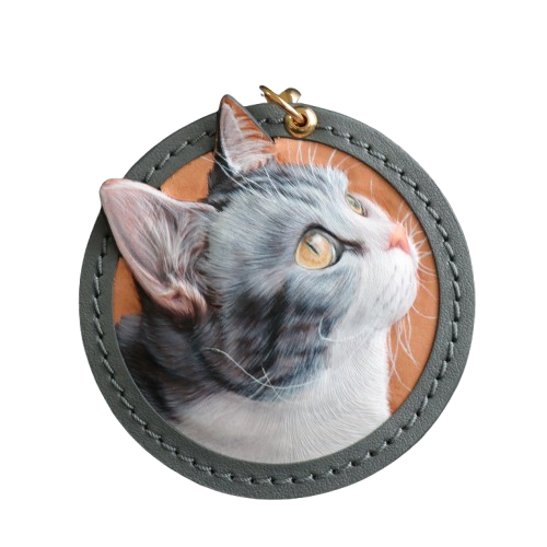 A handcrafted round leather keychain featuring a detailed, lifelike portrait of a grey and white cat with yellow eyes, beautifully capturing the pet's inquisitive expression. The craftsmanship highlights the artist’s attention to detail, making this a perfect personalized gift for cat lovers.