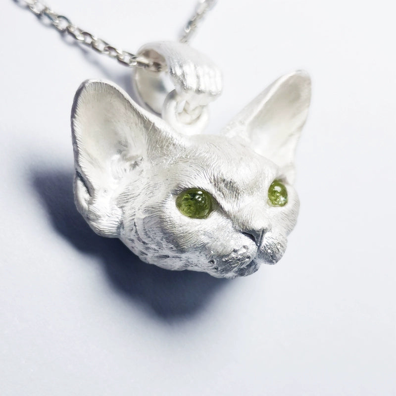 This image showcases the Devon Bobcat Silver Pendant, a beautifully handcrafted pet memorial necklace made from 925 sterling silver. The pendant features lifelike details of the Devon Bobcat, with carefully set gemstone eyes that add a unique touch. Due to the handcrafted nature, each piece has slight variations, making it one-of-a-kind. Custom engraving is available to personalize the pendant as a cherished keepsake. The image highlights the fine craftsmanship and delicate details that make this pendan