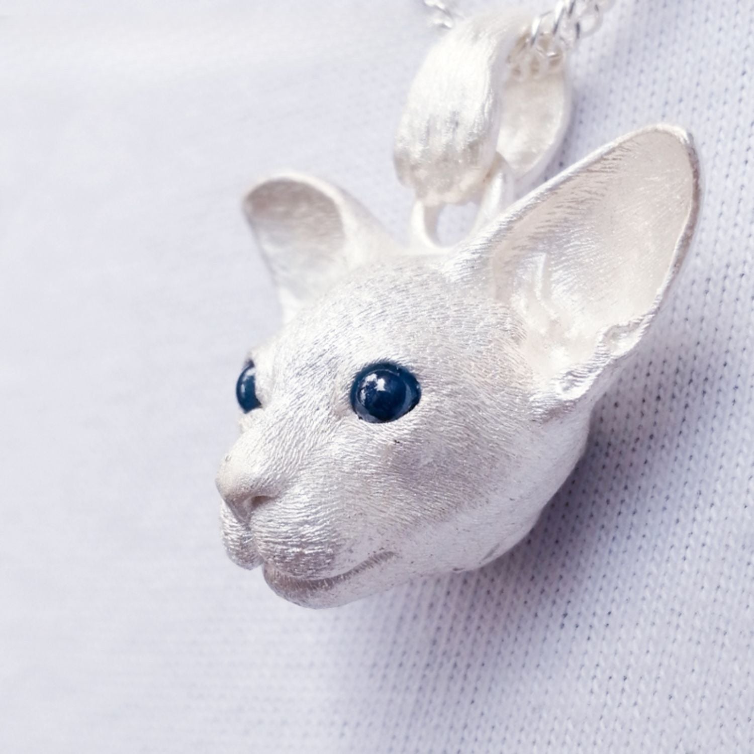 Close-up image of the East Short Abbey Cat Pendant, handcrafted from 925 pure silver with detailed cat features and gemstone eyes. Available in silver and antique black finishes, this pendant can be personalized with custom engraving to honor your pet’s memory.