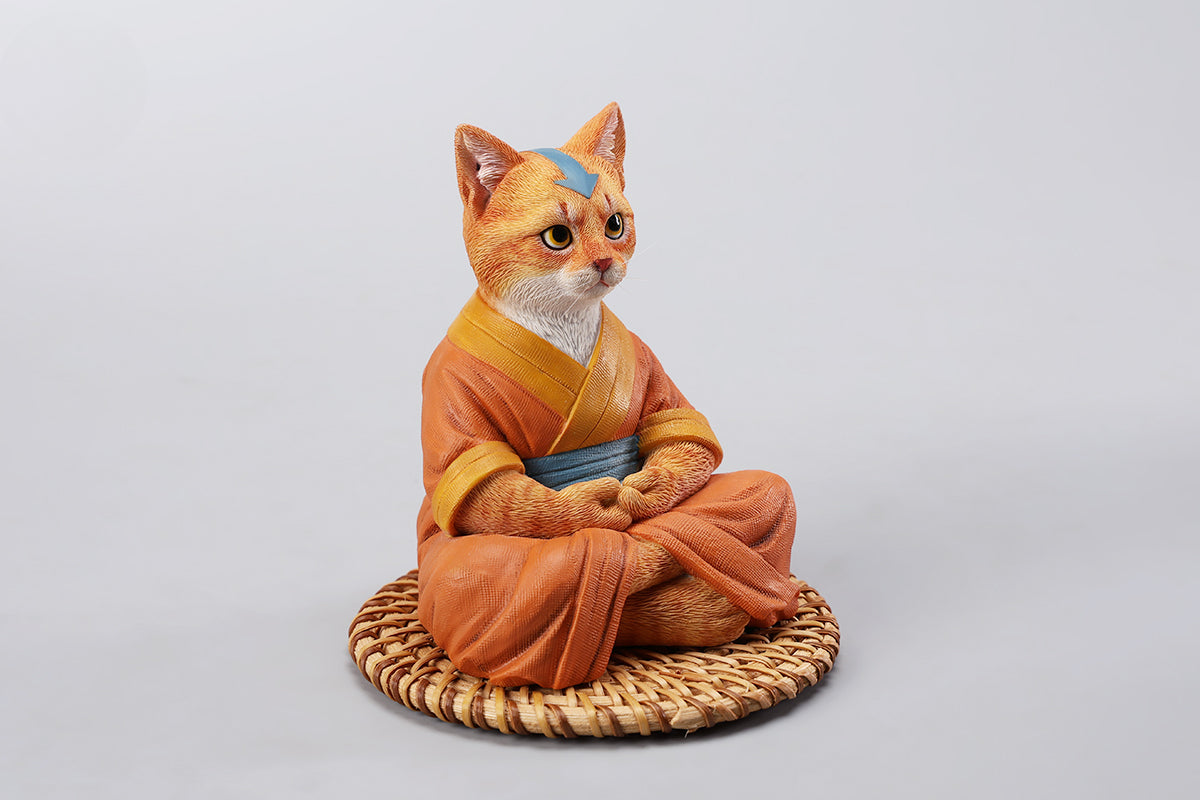 A handcrafted Airbender Cat Figurine in a meditative pose, dressed in an orange robe with a blue sash, sitting on a rattan-weaved cushion. This finely detailed resin sculpture captures the tranquility of mindfulness, perfect for cat lovers and meditation enthusiasts. An ideal collectible and decorative accent for any serene space.