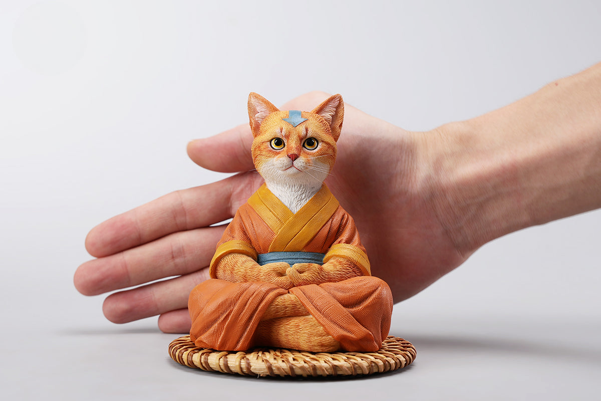 A handcrafted Airbender Cat Figurine in a meditative pose, dressed in an orange robe with a blue sash, sitting on a rattan-weaved cushion. This finely detailed resin sculpture captures the tranquility of mindfulness, perfect for cat lovers and meditation enthusiasts. An ideal collectible and decorative accent for any serene space.