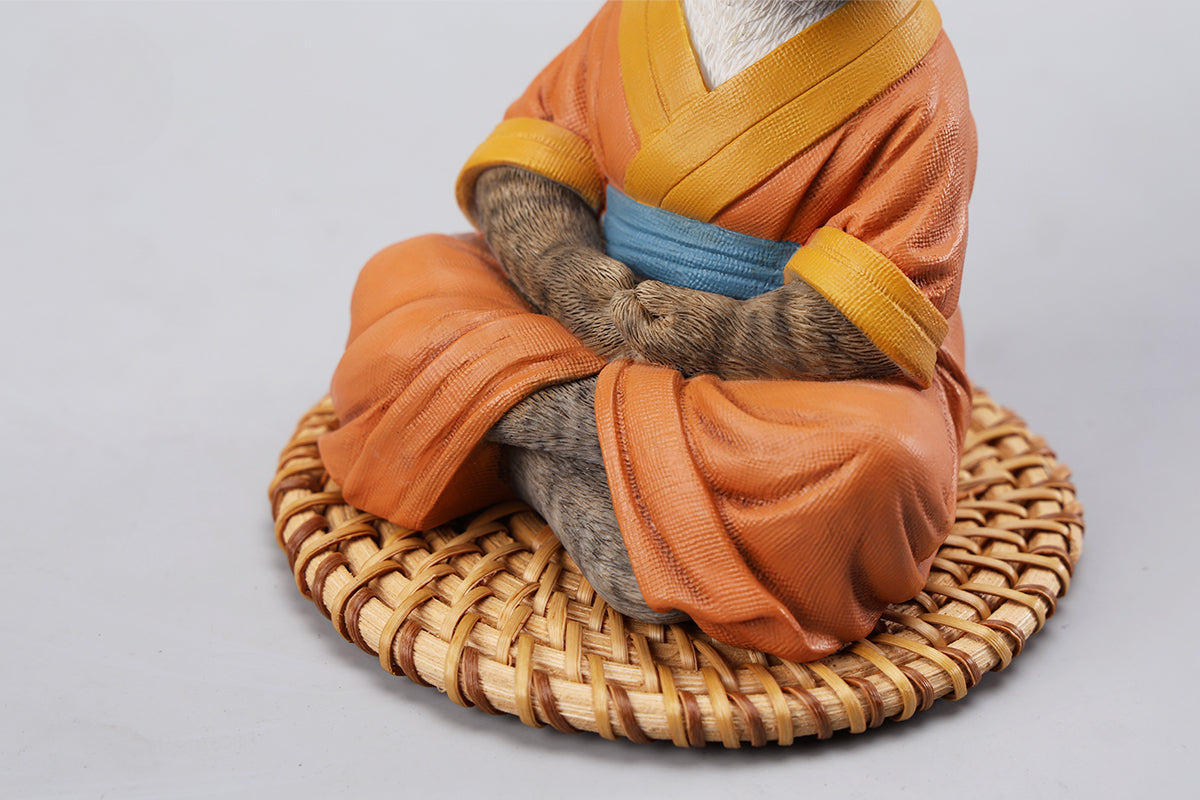 A handcrafted Airbender Cat Figurine in a meditative pose, dressed in an orange robe with a blue sash, sitting on a rattan-weaved cushion. This finely detailed resin sculpture captures the tranquility of mindfulness, perfect for cat lovers and meditation enthusiasts. An ideal collectible and decorative accent for any serene space.