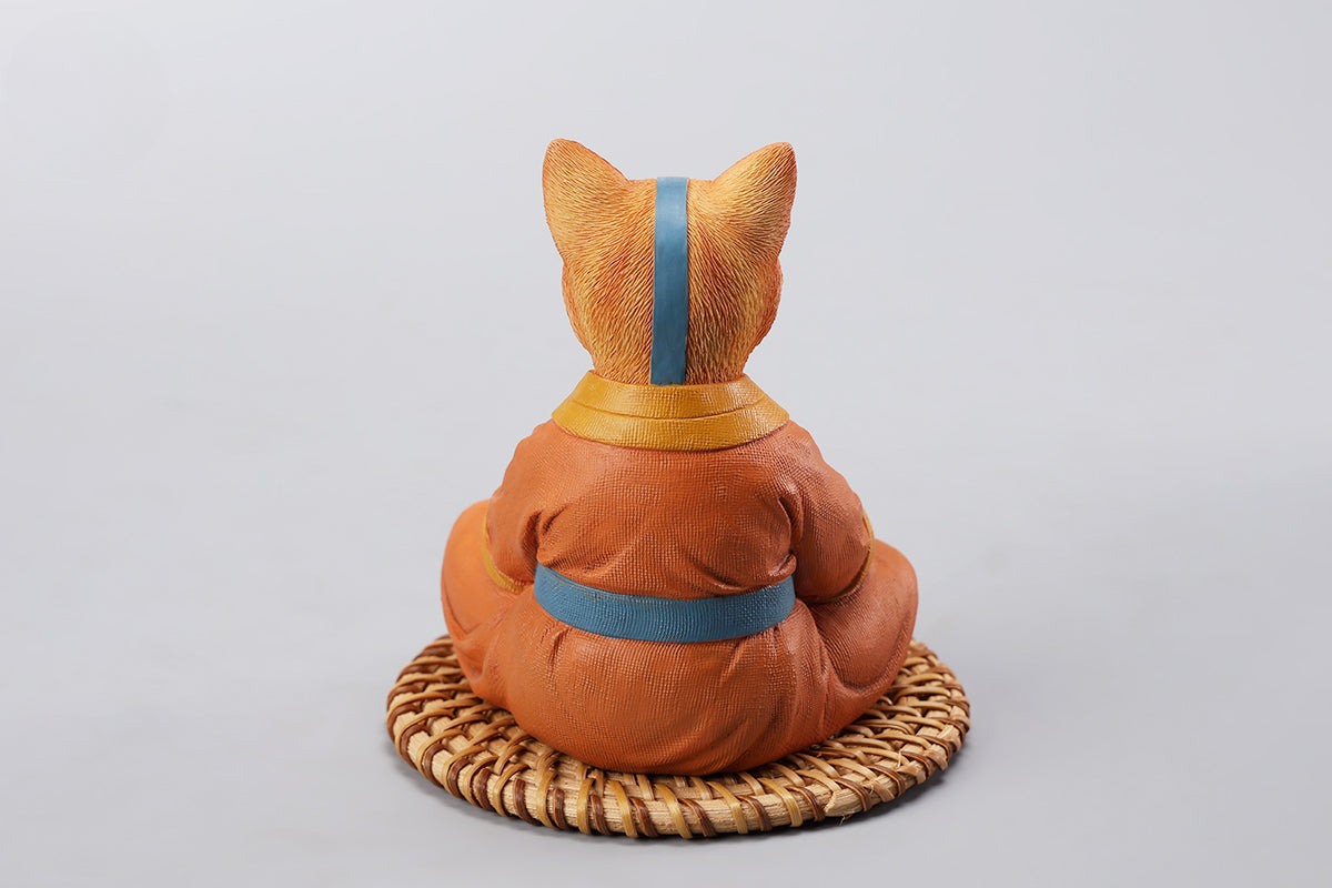 A handcrafted Airbender Cat Figurine in a meditative pose, dressed in an orange robe with a blue sash, sitting on a rattan-weaved cushion. This finely detailed resin sculpture captures the tranquility of mindfulness, perfect for cat lovers and meditation enthusiasts. An ideal collectible and decorative accent for any serene space.