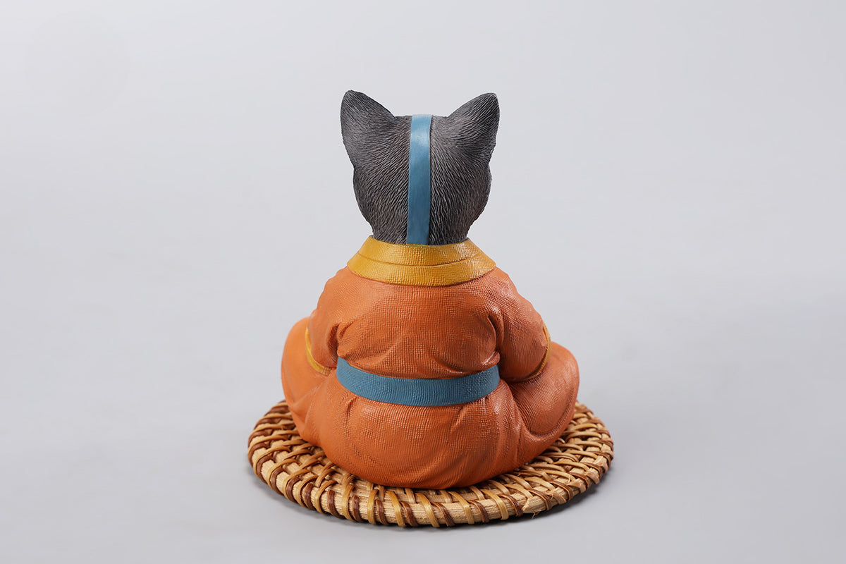 A handcrafted Airbender Cat Figurine in a meditative pose, dressed in an orange robe with a blue sash, sitting on a rattan-weaved cushion. This finely detailed resin sculpture captures the tranquility of mindfulness, perfect for cat lovers and meditation enthusiasts. An ideal collectible and decorative accent for any serene space.