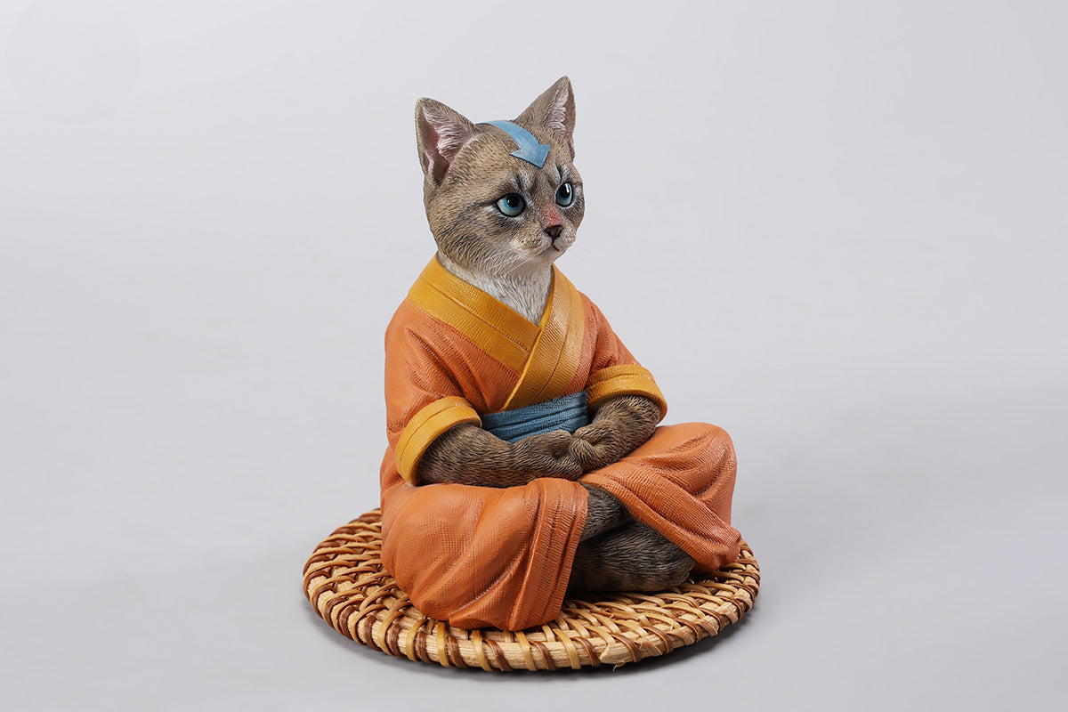 A handcrafted Airbender Cat Figurine in a meditative pose, dressed in an orange robe with a blue sash, sitting on a rattan-weaved cushion. This finely detailed resin sculpture captures the tranquility of mindfulness, perfect for cat lovers and meditation enthusiasts. An ideal collectible and decorative accent for any serene space.