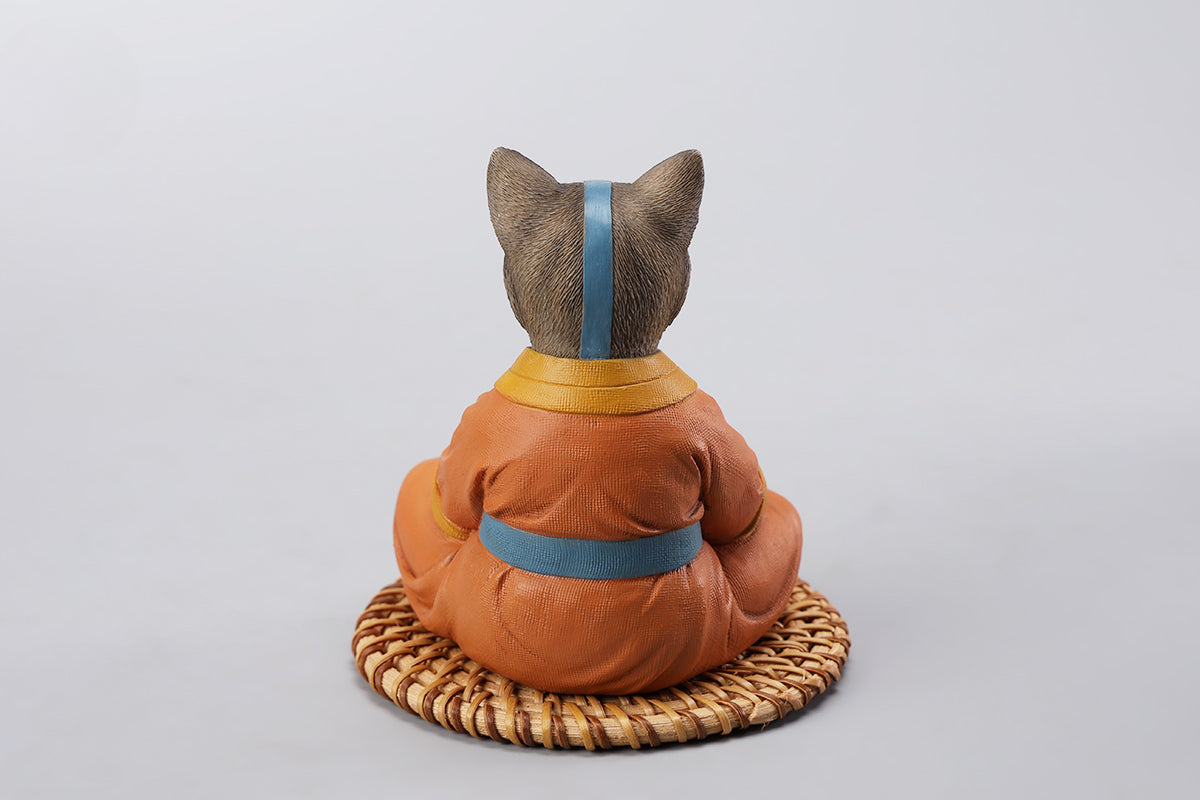 A handcrafted Airbender Cat Figurine in a meditative pose, dressed in an orange robe with a blue sash, sitting on a rattan-weaved cushion. This finely detailed resin sculpture captures the tranquility of mindfulness, perfect for cat lovers and meditation enthusiasts. An ideal collectible and decorative accent for any serene space.