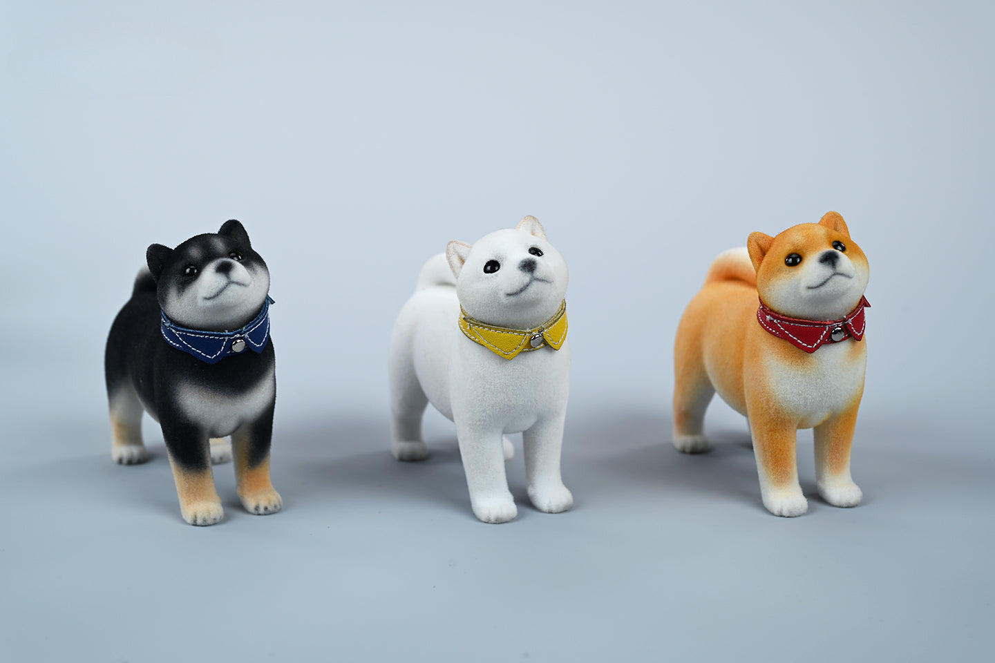 A set of three flocking Shiba Inu dog models in different colors - black, white, and tan. Each model features a realistic and adorable design with a collar in different colors: blue, yellow, and red. The dogs are shown in various poses, including waving, standing, and sitting.