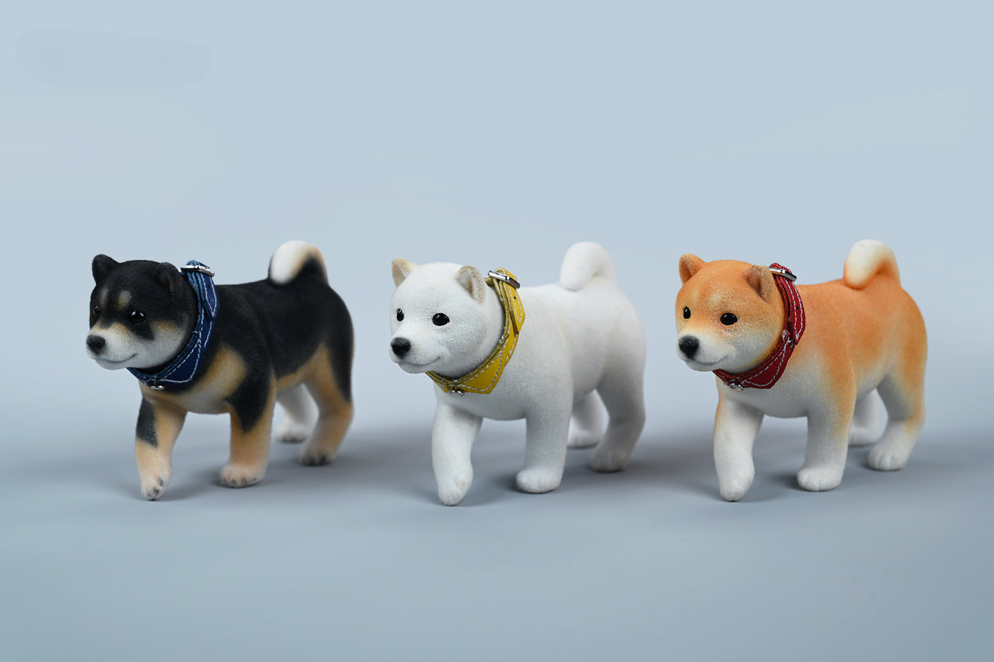 A set of three flocking Shiba Inu dog models in different colors - black, white, and tan. Each model features a realistic and adorable design with a collar in different colors: blue, yellow, and red. The dogs are shown in various poses, including waving, standing, and sitting.