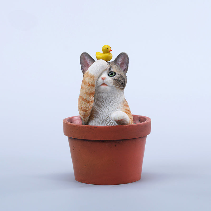 This charming Flower Pot Cat Model features a playful kitten peeking out of a terracotta pot with a small yellow rubber duck on its head. The series includes multiple variations, each with a different accessory atop the cat's head. This delightful ornament brings a touch of whimsy and cheer to any space, perfect for cat lovers and collectors alike. The detailed craftsmanship and vibrant colors make it a standout piece in any collection.