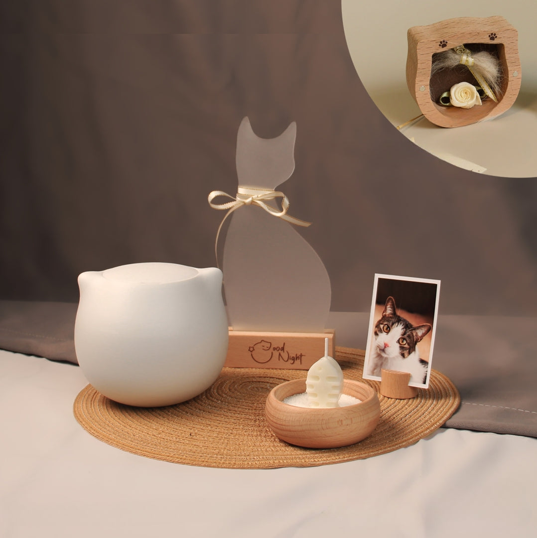 White ceramic cat-shaped pet cremation urn set with personalized memorial plaque, candle holder, fur keepsake box, photo stand, and woven mat, designed for home ashes storage and display.