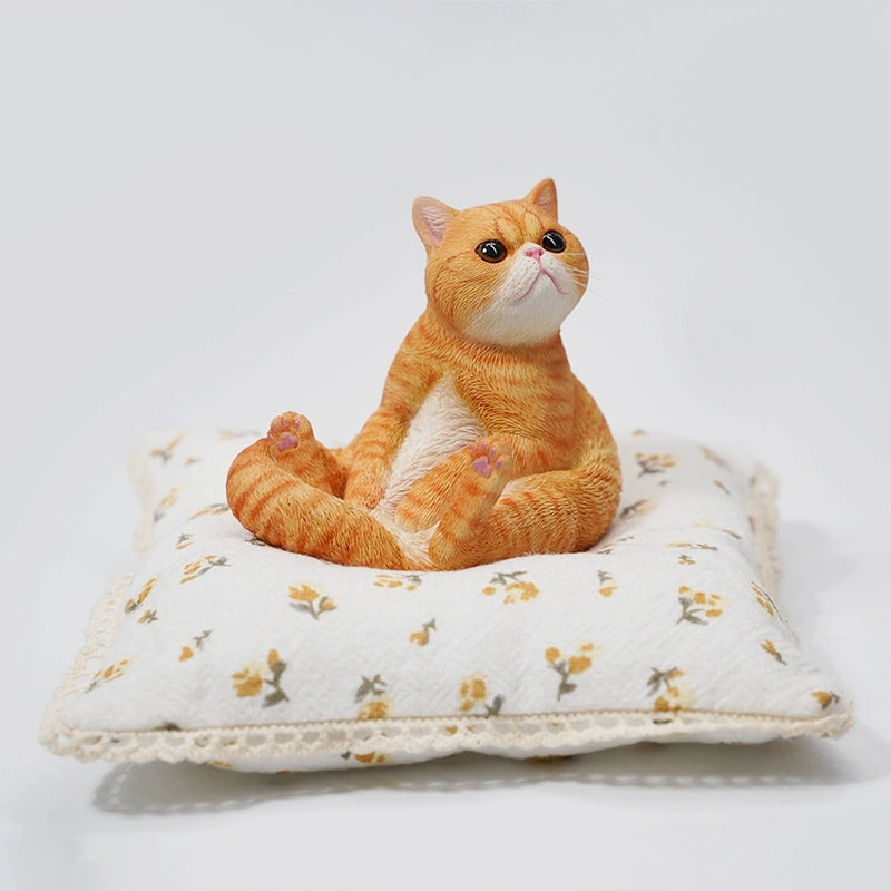 This image showcases a 1/6 Lazy Cat 8.0 Model, featuring an orange cat figurine sitting on a soft, floral-patterned cushion. The cat is in a relaxed pose, with its tail curled around its body and its front paws resting on its belly. The detailed design captures the cat's lifelike features, including its expressive eyes and realistic fur texture.