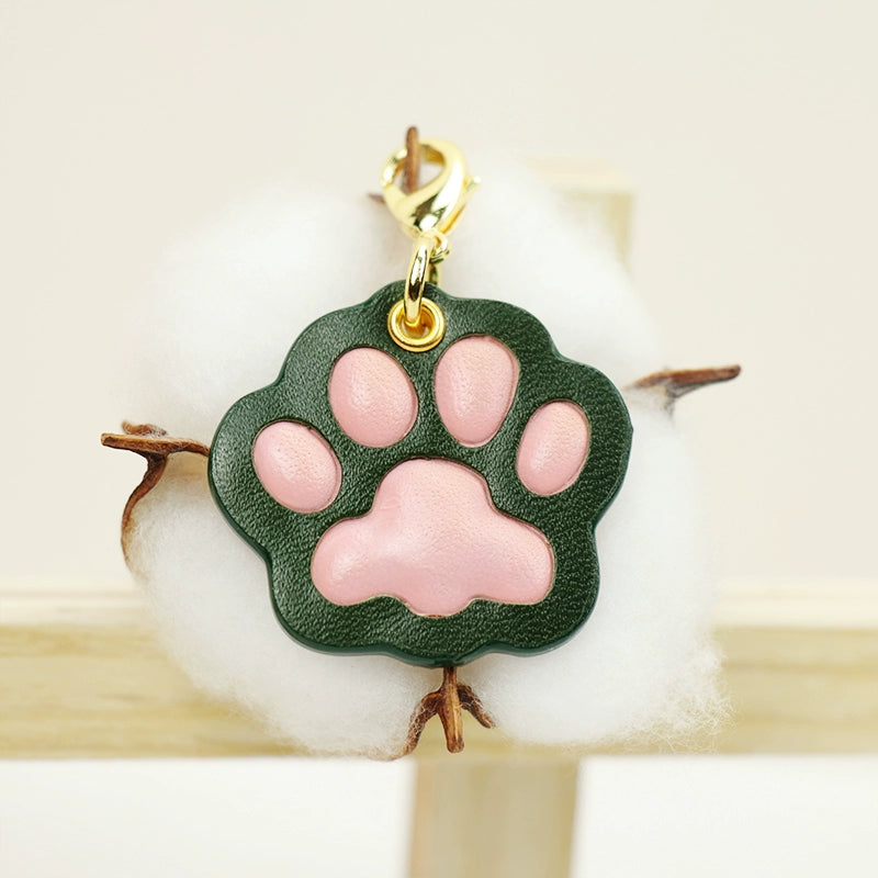 A collection of four handcrafted leather paw-shaped pendants in various colors, including black, green, tan, and white. Each pendant features a contrasting paw print, highlighting the high-quality craftsmanship and customizable options available. Ideal for pet owners who appreciate unique and personalized accessories.