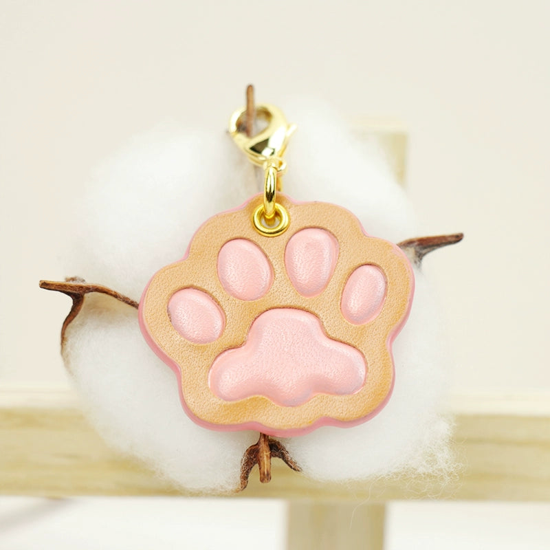 A collection of four handcrafted leather paw-shaped pendants in various colors, including black, green, tan, and white. Each pendant features a contrasting paw print, highlighting the high-quality craftsmanship and customizable options available. Ideal for pet owners who appreciate unique and personalized accessories.