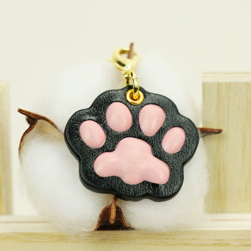 A collection of four handcrafted leather paw-shaped pendants in various colors, including black, green, tan, and white. Each pendant features a contrasting paw print, highlighting the high-quality craftsmanship and customizable options available. Ideal for pet owners who appreciate unique and personalized accessories.