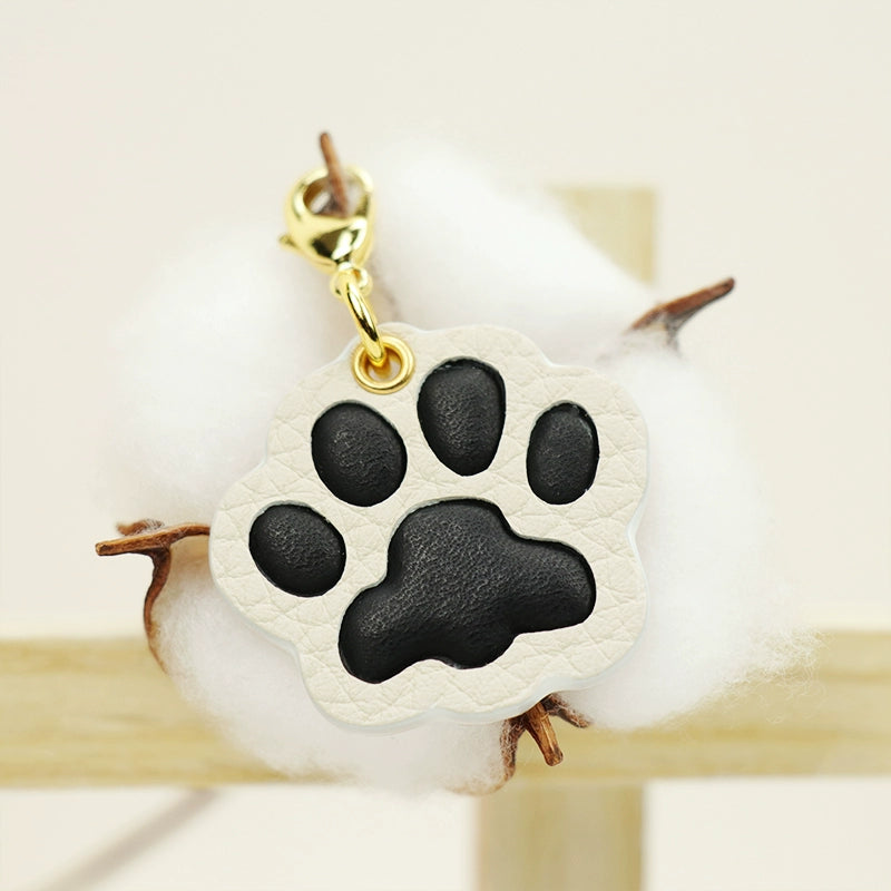 A collection of four handcrafted leather paw-shaped pendants in various colors, including black, green, tan, and white. Each pendant features a contrasting paw print, highlighting the high-quality craftsmanship and customizable options available. Ideal for pet owners who appreciate unique and personalized accessories.