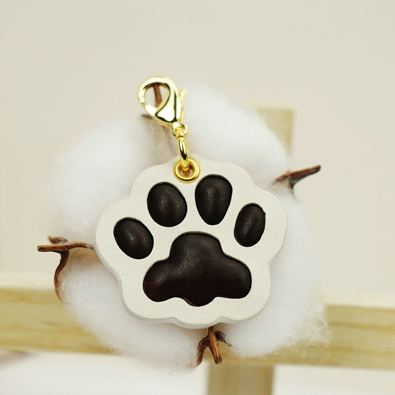 A collection of four handcrafted leather paw-shaped pendants in various colors, including black, green, tan, and white. Each pendant features a contrasting paw print, highlighting the high-quality craftsmanship and customizable options available. Ideal for pet owners who appreciate unique and personalized accessories.