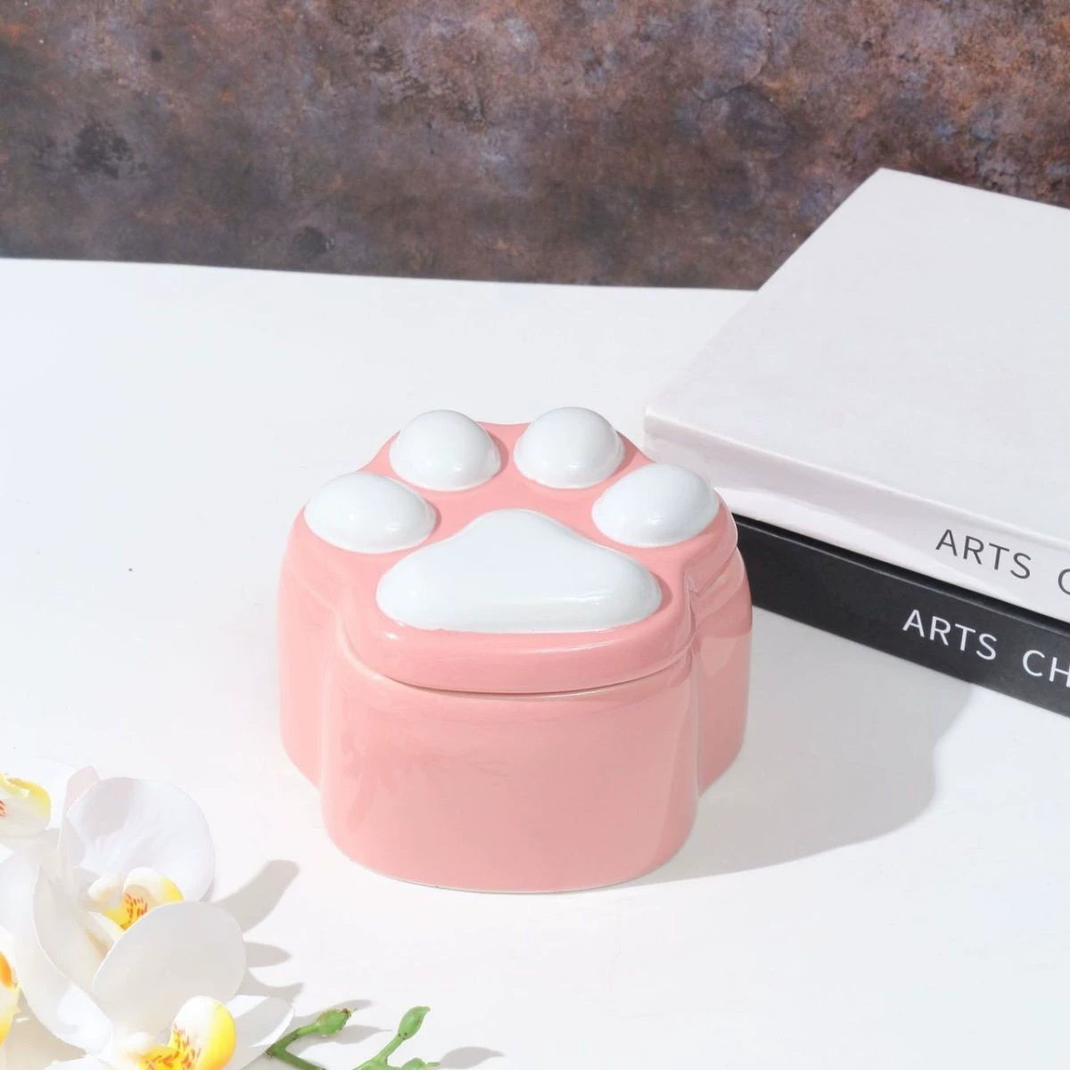 This pink and black paw ceramic pet urn features a stylish paw print lid, available in soft pink or sleek black, measuring approximately 12cm tall and 10cm wide. Crafted from durable ceramic, it offers secure storage for ashes of small to medium pets like cats or dogs, making it a heartfelt memorial display for North American pet owners on shelves or tables.