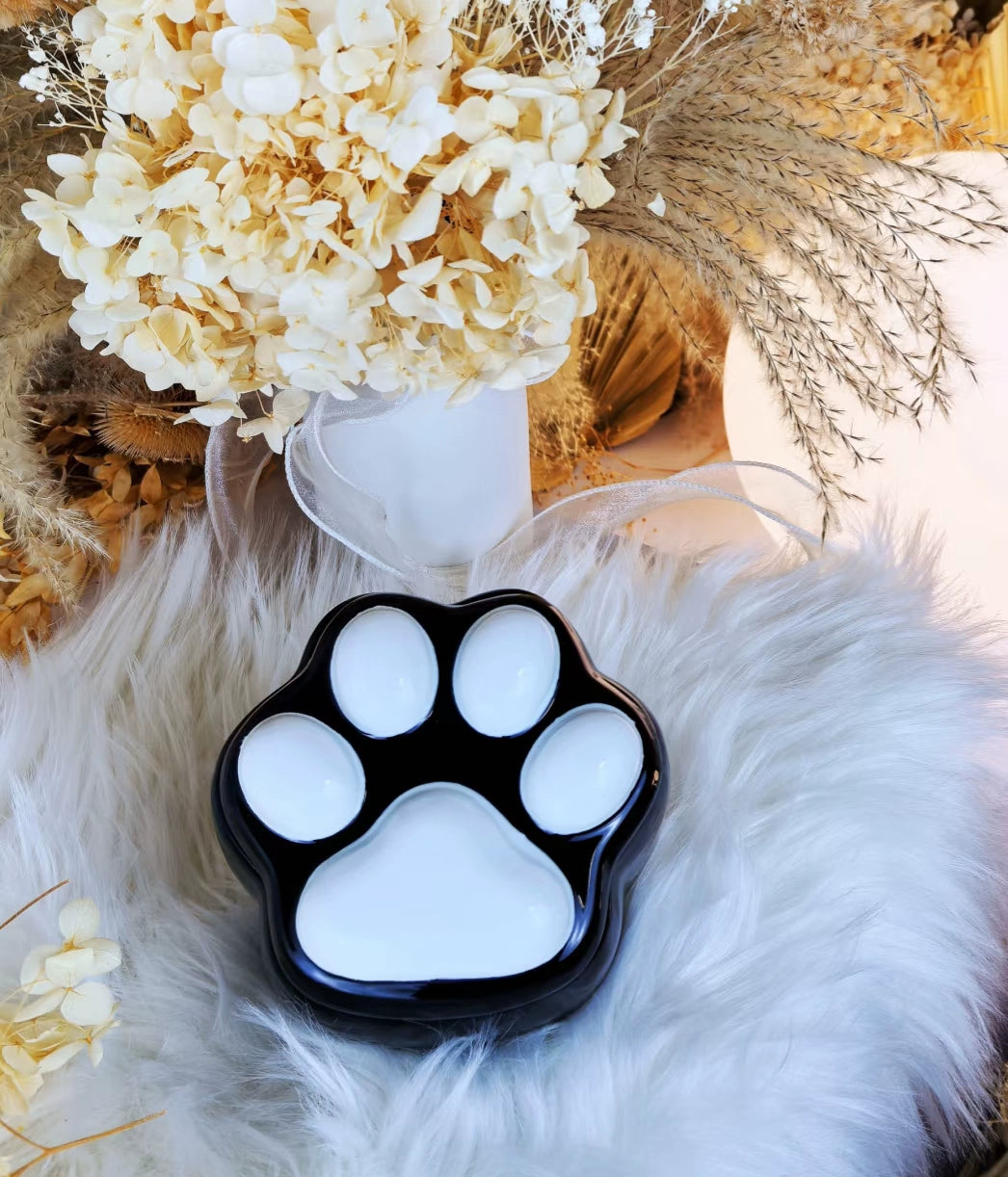 This pink and black paw ceramic pet urn features a stylish paw print lid, available in soft pink or sleek black, measuring approximately 12cm tall and 10cm wide. Crafted from durable ceramic, it offers secure storage for ashes of small to medium pets like cats or dogs, making it a heartfelt memorial display for North American pet owners on shelves or tables.