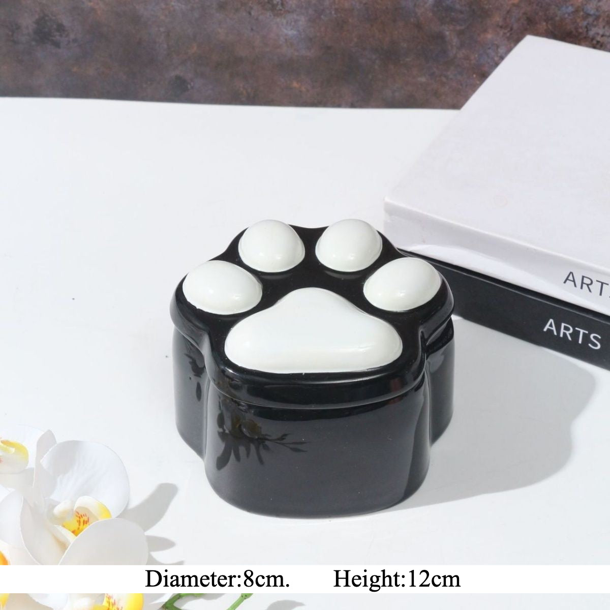 This pink and black paw ceramic pet urn features a stylish paw print lid, available in soft pink or sleek black, measuring approximately 12cm tall and 10cm wide. Crafted from durable ceramic, it offers secure storage for ashes of small to medium pets like cats or dogs, making it a heartfelt memorial display for North American pet owners on shelves or tables.