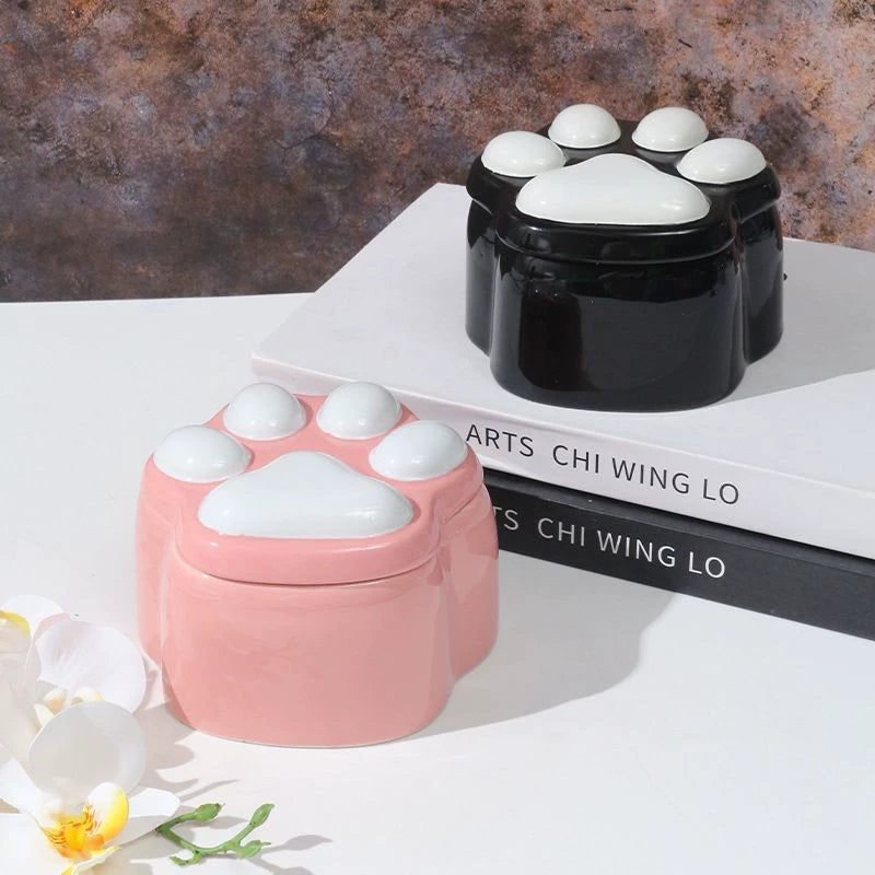 This pink and black paw ceramic pet urn features a stylish paw print lid, available in soft pink or sleek black, measuring approximately 12cm tall and 10cm wide. Crafted from durable ceramic, it offers secure storage for ashes of small to medium pets like cats or dogs, making it a heartfelt memorial display for North American pet owners on shelves or tables.