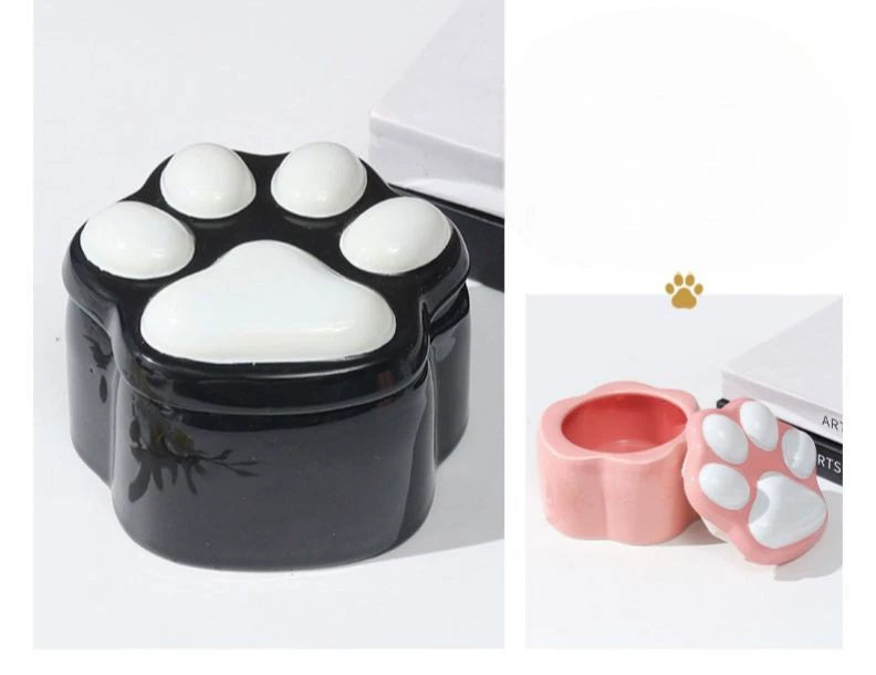 This pink and black paw ceramic pet urn features a stylish paw print lid, available in soft pink or sleek black, measuring approximately 12cm tall and 10cm wide. Crafted from durable ceramic, it offers secure storage for ashes of small to medium pets like cats or dogs, making it a heartfelt memorial display for North American pet owners on shelves or tables.