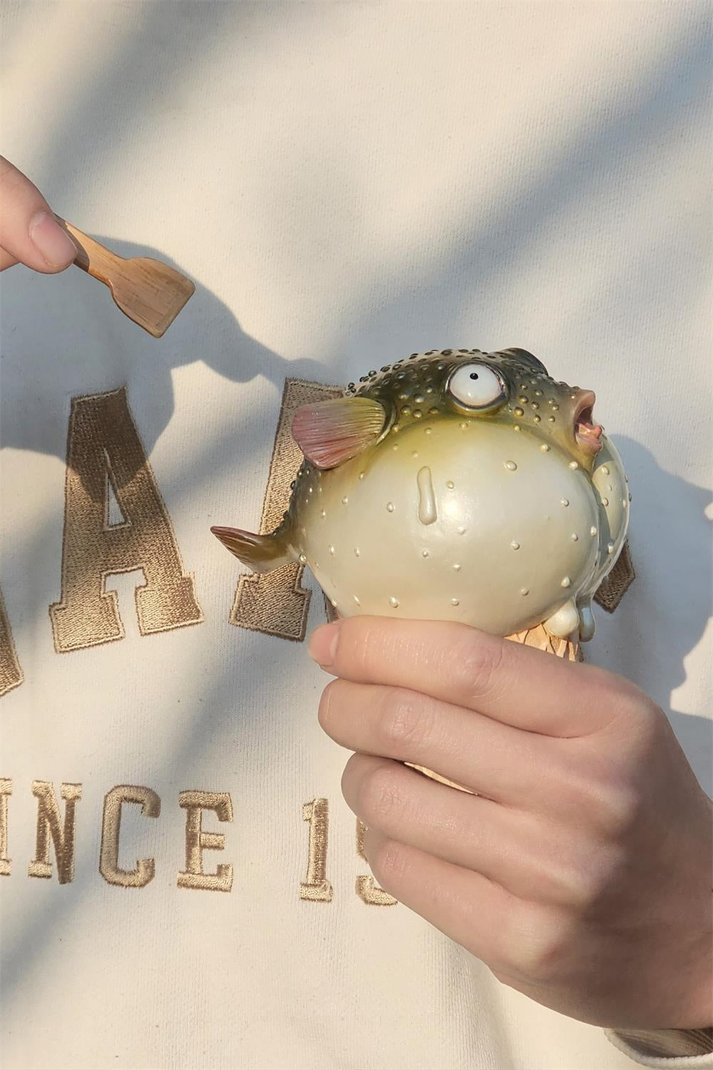 A highly detailed pufferfish ice cream figurine featuring a realistic fish with bulging eyes and textured scales, sitting on an intricately sculpted ice cream cone base. Made of premium resin, this collectible novelty item is perfect for unique decor lovers and marine life enthusiasts.