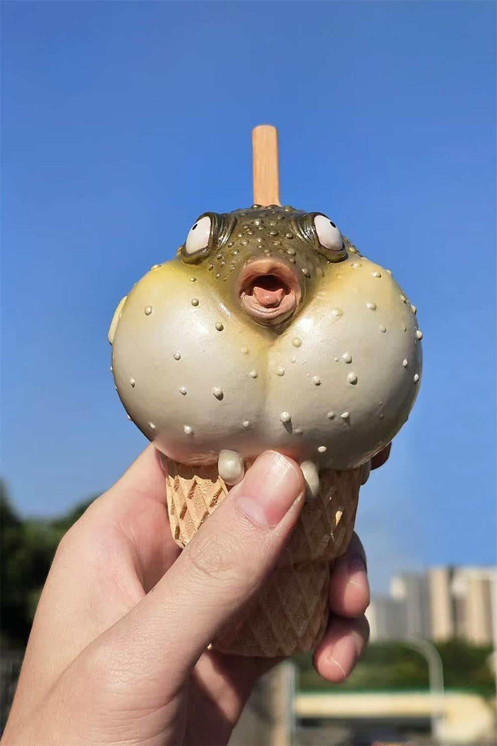 A highly detailed pufferfish ice cream figurine featuring a realistic fish with bulging eyes and textured scales, sitting on an intricately sculpted ice cream cone base. Made of premium resin, this collectible novelty item is perfect for unique decor lovers and marine life enthusiasts.