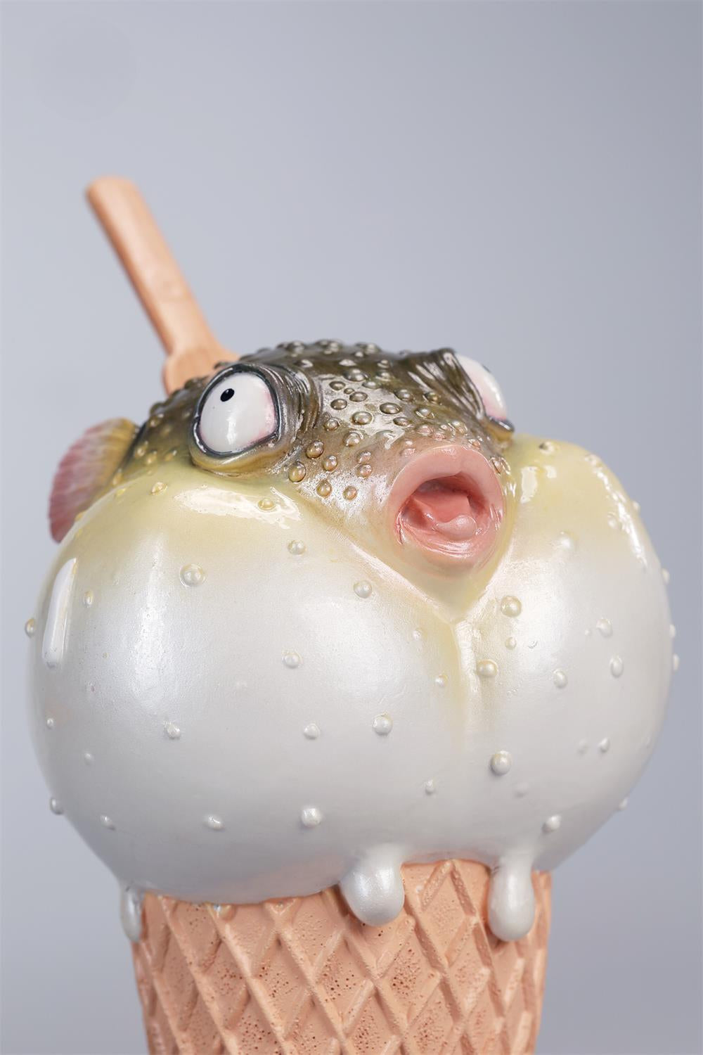A highly detailed pufferfish ice cream figurine featuring a realistic fish with bulging eyes and textured scales, sitting on an intricately sculpted ice cream cone base. Made of premium resin, this collectible novelty item is perfect for unique decor lovers and marine life enthusiasts.